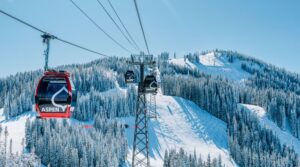 Teleférico de gôndola vermelha com o logotipo Aspen sobrevoando a montanha Ajax coberta de neve e pinheiros em Aspen Snowmass, Colorado, durante a temporada de esqui 2026 2027.