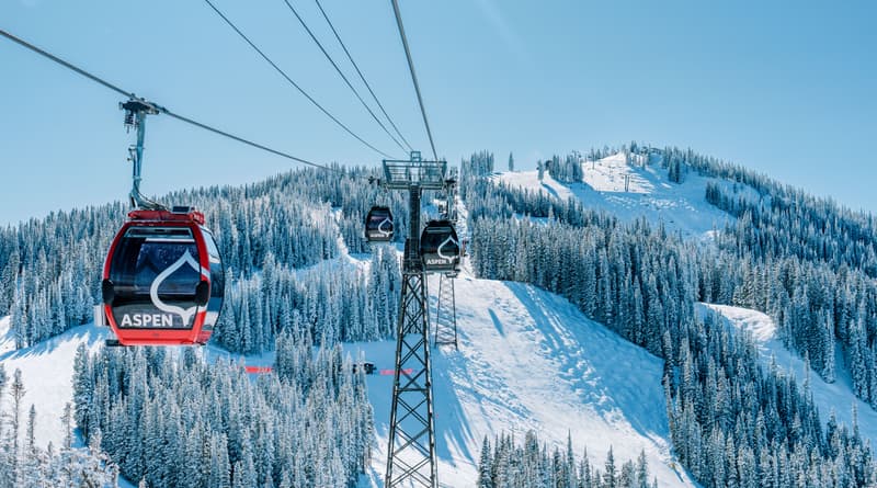 Teleférico de gôndola vermelha com o logotipo Aspen sobrevoando a montanha Ajax coberta de neve e pinheiros em Aspen Snowmass, Colorado, durante a temporada de esqui 2026 2027.