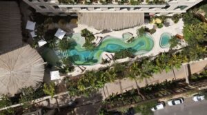 Vista aérea da piscina orgânica de águas verdes do Hotel Rosewood São Paulo, na Cidade Matarazzo, cercada por vegetação tropical, espreguiçadeiras e guarda-sóis, resort urbano premiado com três chaves Michelin.