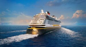 Navio Disney Believe da Disney Cruise Line navegando em mar aberto com casco branco e detalhes dourados, anúncio oficial do novo navio da classe Wish com viagem inaugural em 18 de dezembro de 2027 saindo de Fort Lauderdale.